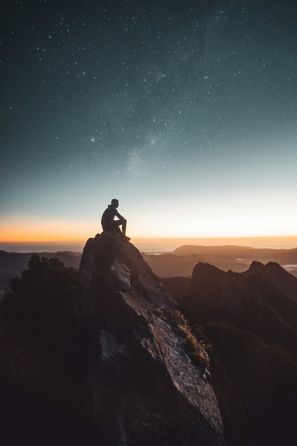 Silhouette einer Person, die während der goldenen Stunde auf einer Felsformation sitzt