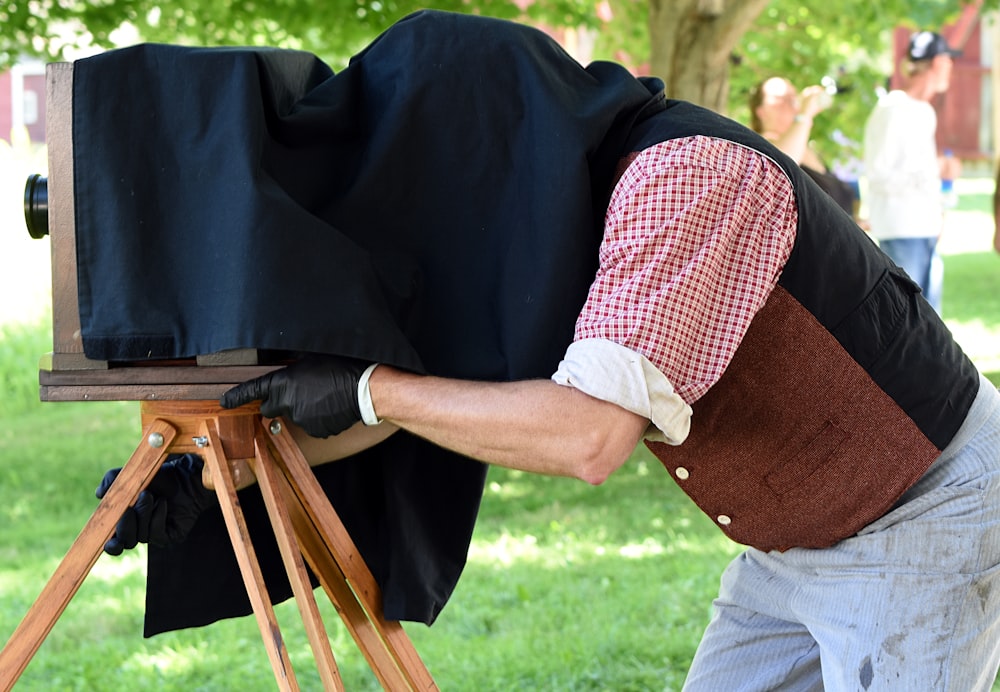 man covering his head with black textile while operating vintage camera