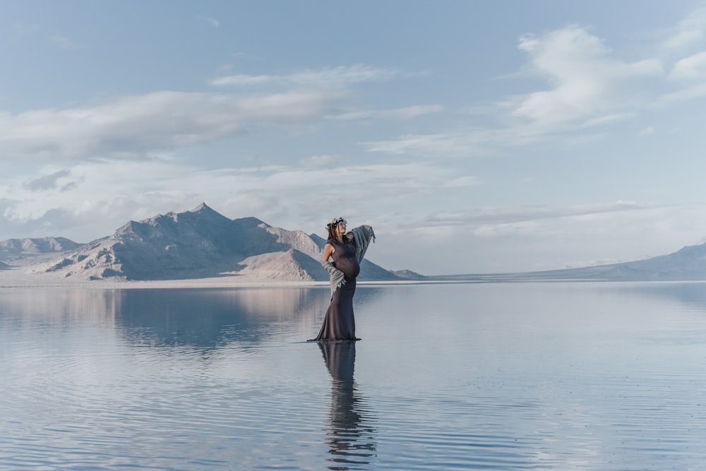 woman standing on body of water with mountains at the distance