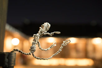 A small wire sculpture appears to depict a human figure in motion, possibly running or jumping. The figure is placed against a softly focused background with warm glowing lights, suggesting an evening or night setting.