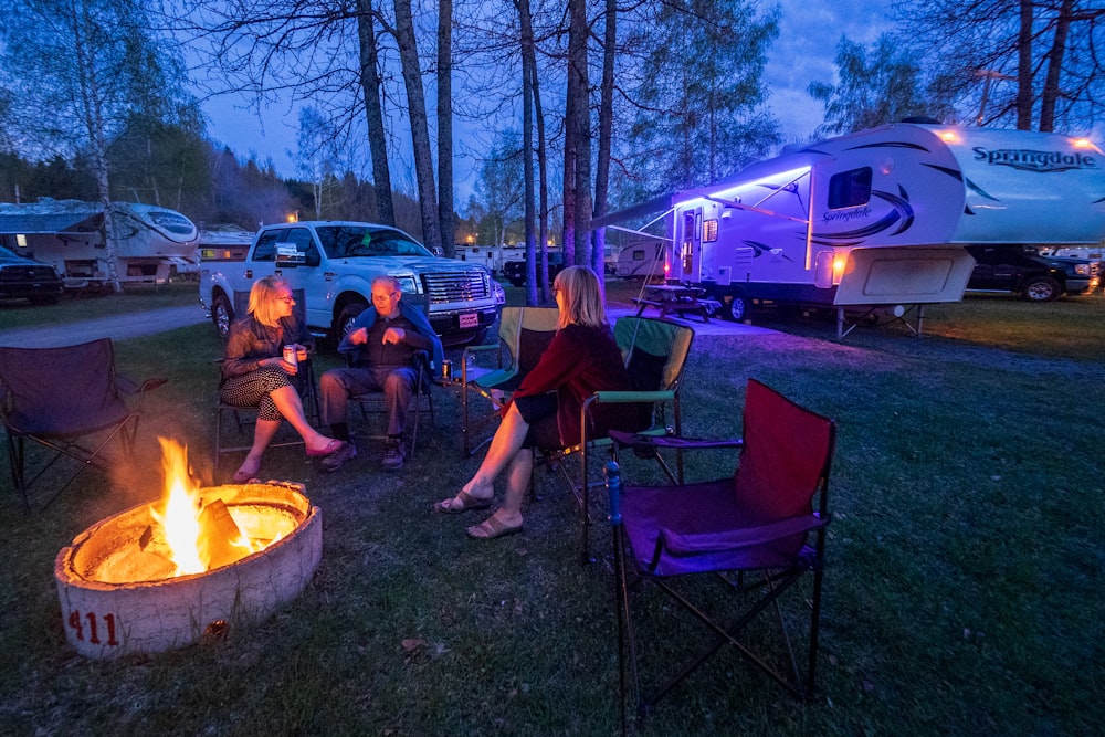 man sitting between two women outside motorhome