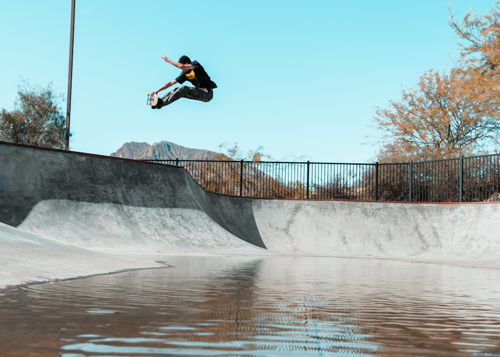 man doing tricks on skateboard in mid air on ramp pit with body of water