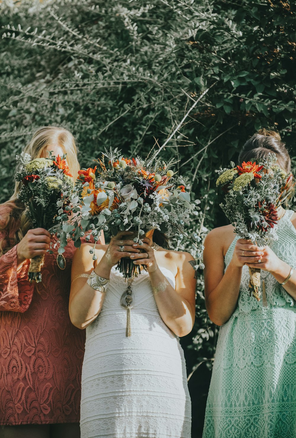 three women covering their faces with bouquet of flowers