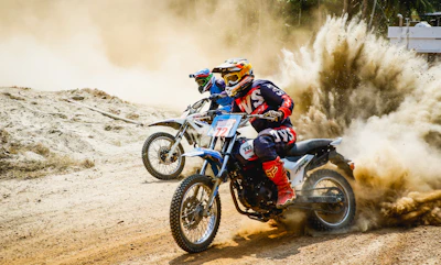 two men riding motocross bikes on brown sand