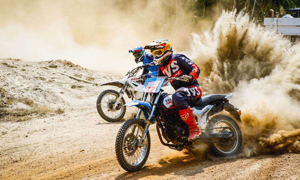 two men riding motocross bikes on brown sand