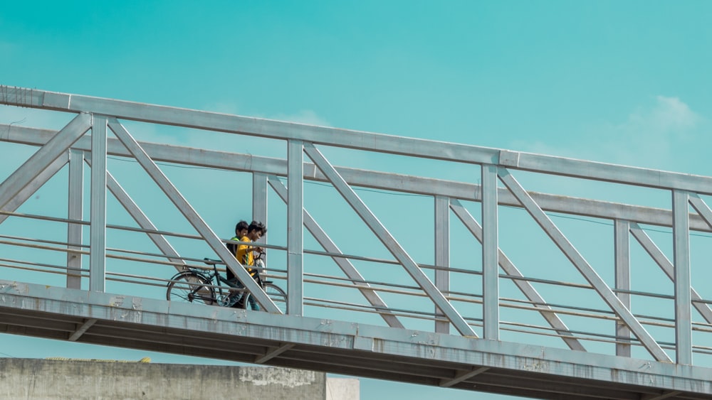 person holding bicycle walking on bridge