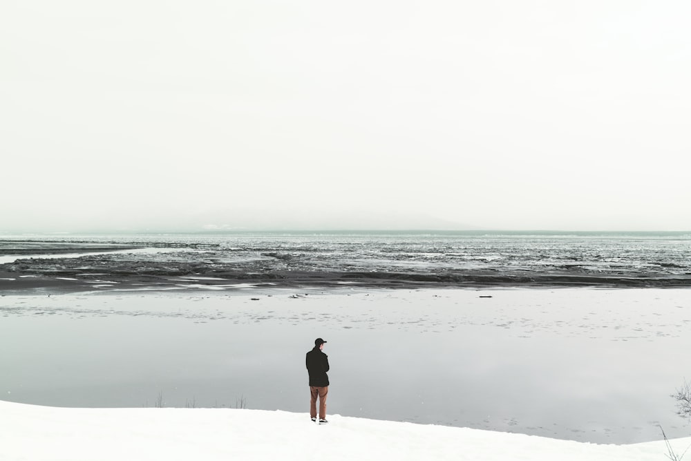 man in black coat standing by the snowy shore