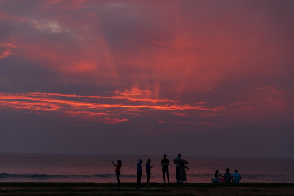 silhouette of people standing and sitting near beach during sunset