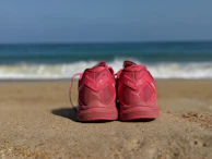 Close-up of aurora branded running shoes on a rocky shore with ocean waves.