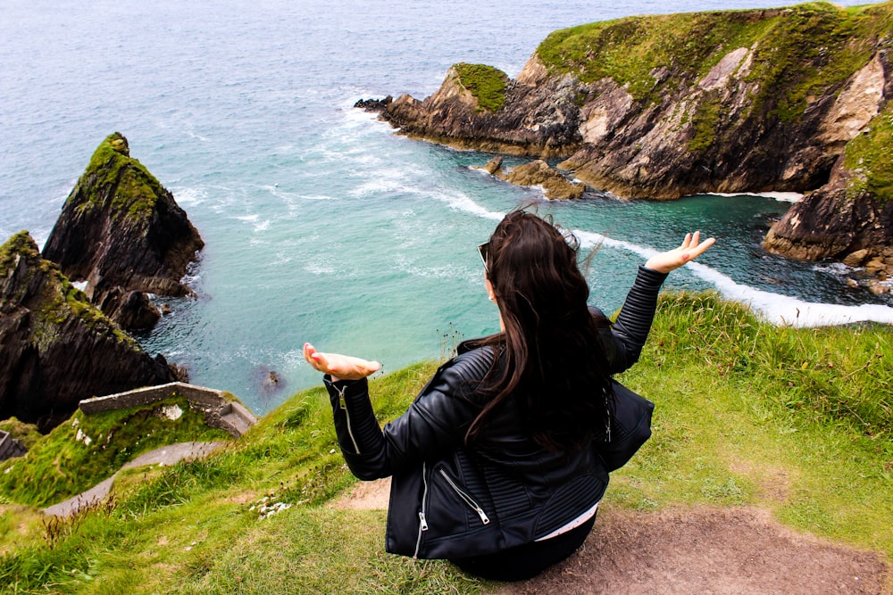 woman sitting on cliff near body of water