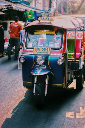 The tuk tuk banana food trailer decorated with bright Thai patterns parked at a sunny market.