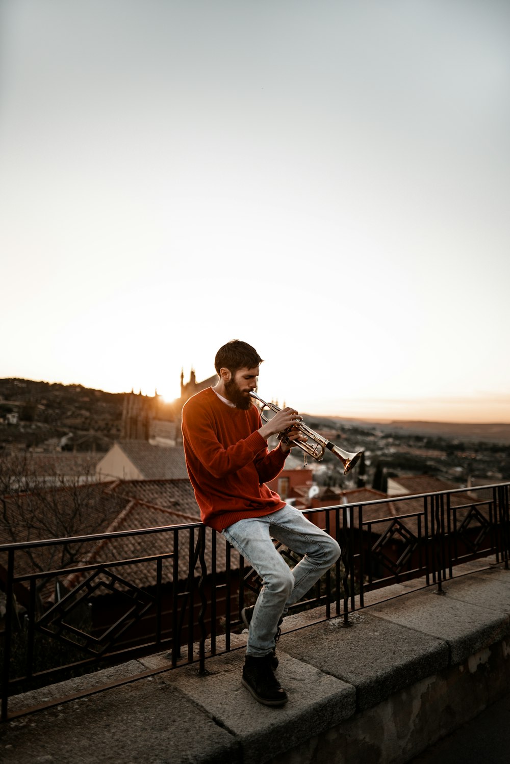 man sitting on railing while playing wind instrument outdoors during daytime