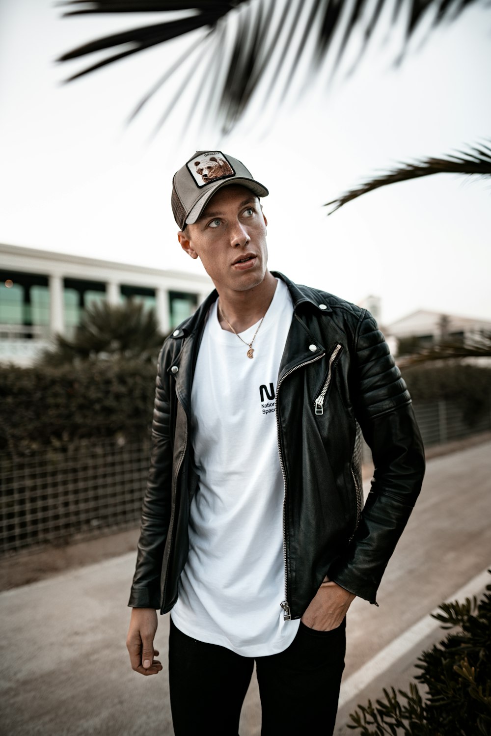 man wearing hat and black leather jacket looks up