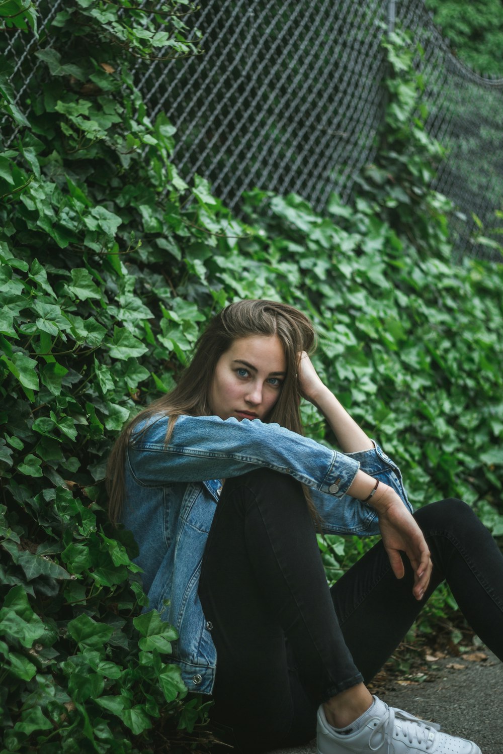 woman sitting against wire fence with crawling vine plants