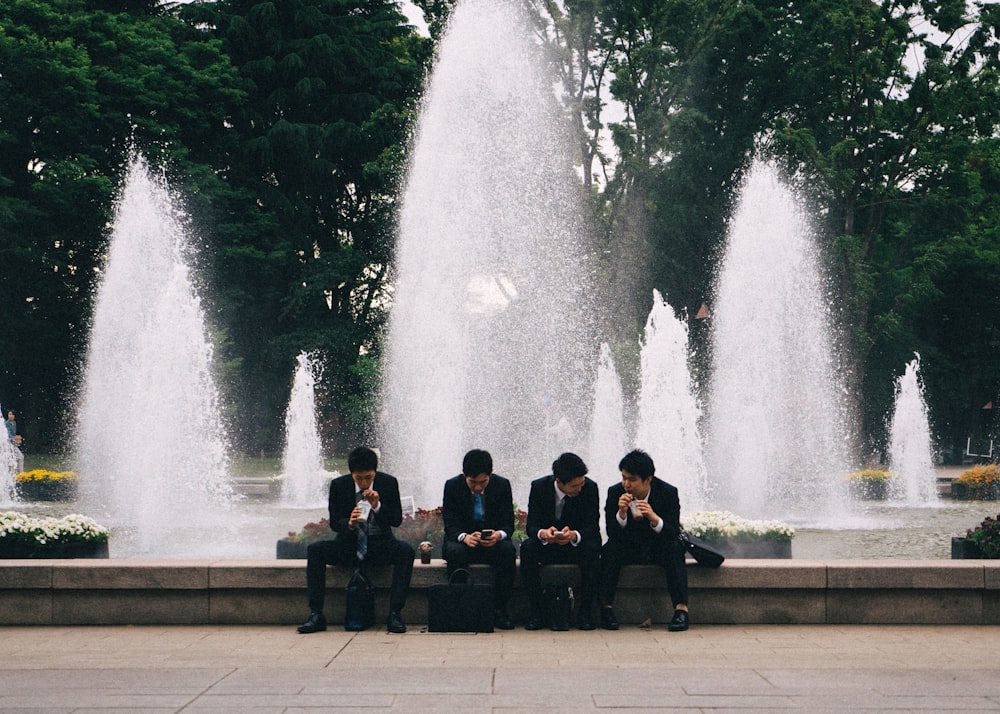 four men sitting near water fountain during daytime