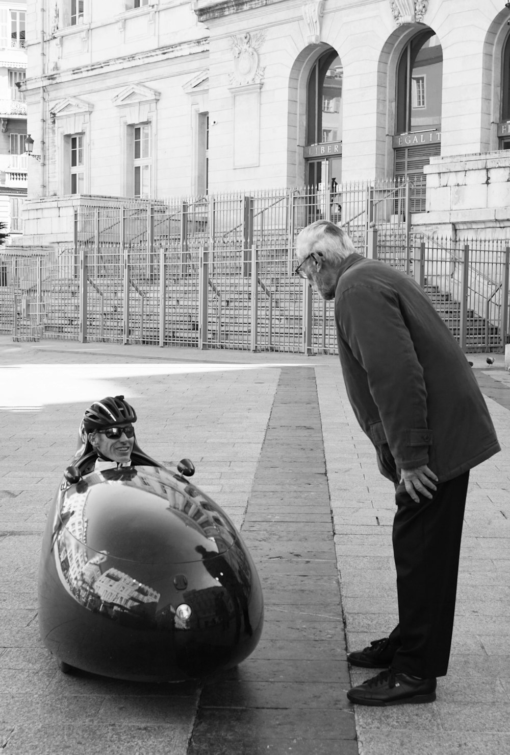 Photographie en niveaux de gris d’un homme debout à côté d’un homme assis sur un mobile