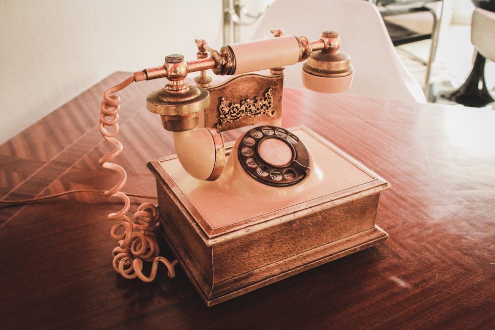 weißes und braunes Wählscheibentelefon auf braunem Holztisch