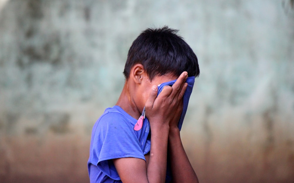 boy in blue shirt covering his face