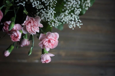Soft pink and white carnations bundled together with rustic twine on a wooden table.