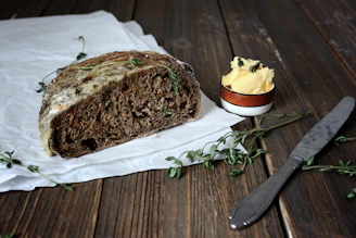 Artisanal bread and cheese spread on a crisp parchment paper, styled with fresh herbs and a matte forest green backdrop.