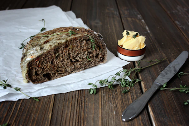 Artisanal bread and cheese spread on a crisp parchment paper, styled with fresh herbs and a matte forest green backdrop.