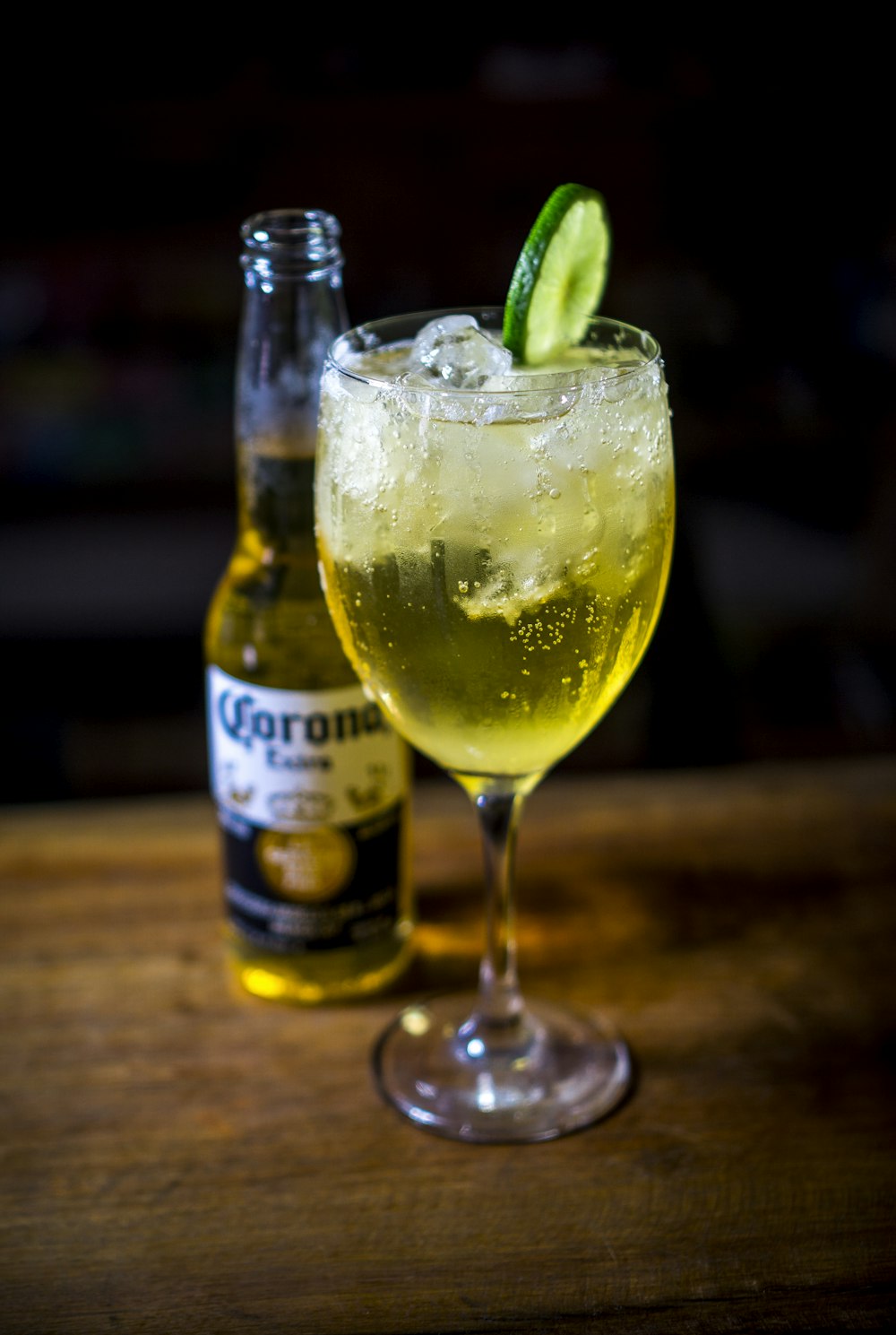 wine glass filled with drink beside Corona beer bottle on brown wooden surface