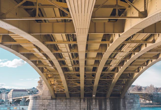 A team applying a protective coating to a large bridge structure under bright daylight.