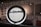 A circular frame with information and images displayed on a screen in a modern interior space. The background includes partial text from a large wall installation and black-and-white photographs. Soft lighting creates a contemporary and sophisticated environment.