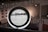 A circular frame with information and images displayed on a screen in a modern interior space. The background includes partial text from a large wall installation and black-and-white photographs. Soft lighting creates a contemporary and sophisticated environment.