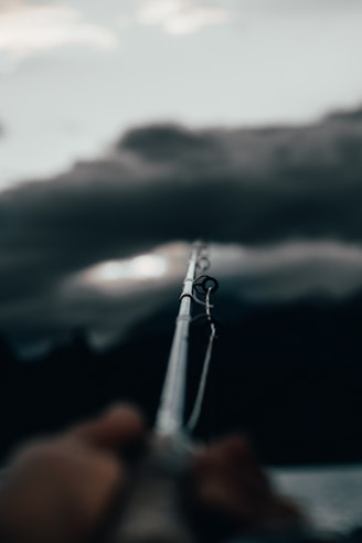 Close-up of a sleek, high-carbon fishing rod held by an angler casting over a calm lake at sunrise.