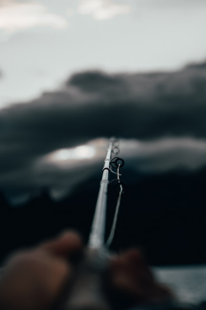 Close-up of a sleek, high-carbon fishing rod held by an angler casting over a calm lake at sunrise.