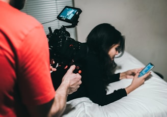 woman holding smartphone while lying on bed near man holding professional camera