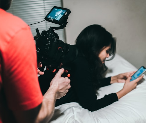 woman holding smartphone while lying on bed near man holding professional camera