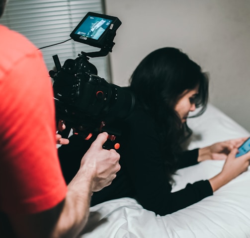 woman holding smartphone while lying on bed near man holding professional camera