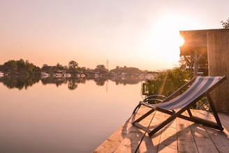 A tranquil lakeside at sunrise with meditation cushions arranged on a wooden deck.