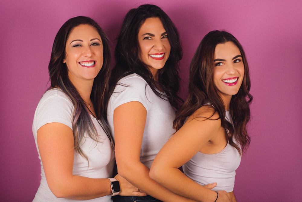 Tres personas con camisas blancas junto a la pared rosa