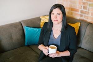 Woman sitting on a brown couch with a coffee cup smiling