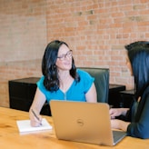 woman in teal t-shirt sitting beside woman in suit jacket