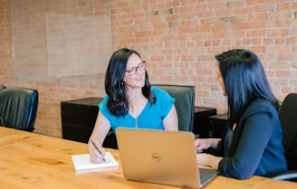 woman in teal t-shirt sitting beside woman in suit jacket