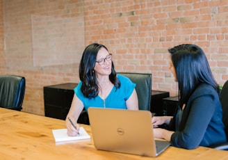 woman in teal t-shirt sitting beside woman in suit jacket