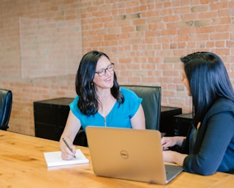 woman in teal t-shirt sitting beside woman in suit jacket