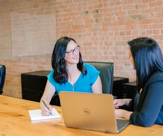 woman in teal t-shirt sitting beside woman in suit jacket