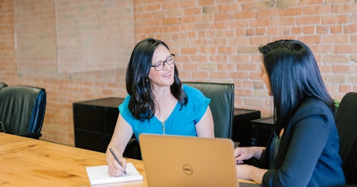 woman in teal t-shirt sitting beside woman in suit jacket