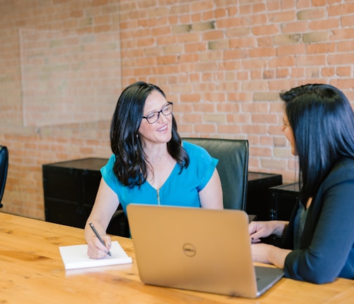 woman in teal t-shirt sitting beside woman in suit jacket