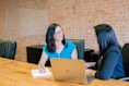 woman in teal t-shirt sitting beside woman in suit jacket