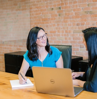 woman in teal t-shirt sitting beside woman in suit jacket