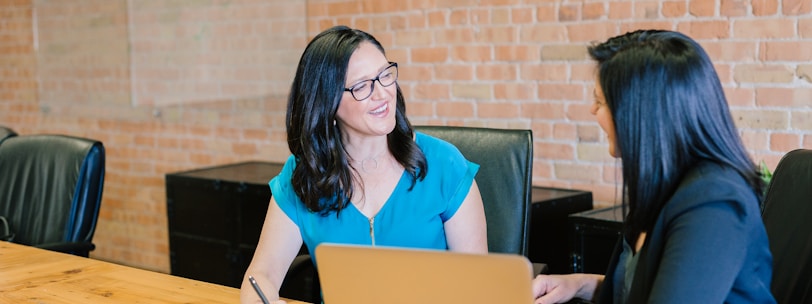 woman in teal t-shirt sitting beside woman in suit jacket