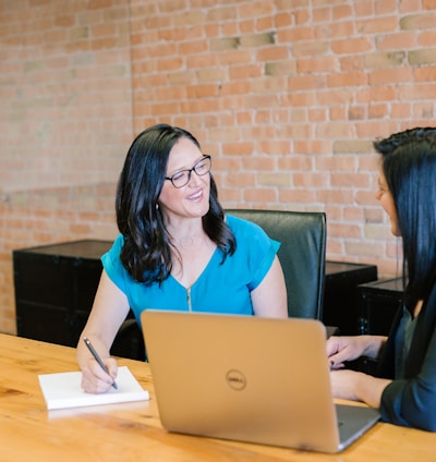 woman in teal t-shirt sitting beside woman in suit jacket