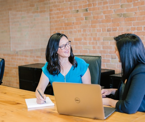 woman in teal t-shirt sitting beside woman in suit jacket