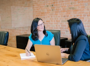 woman in teal t-shirt sitting beside woman in suit jacket